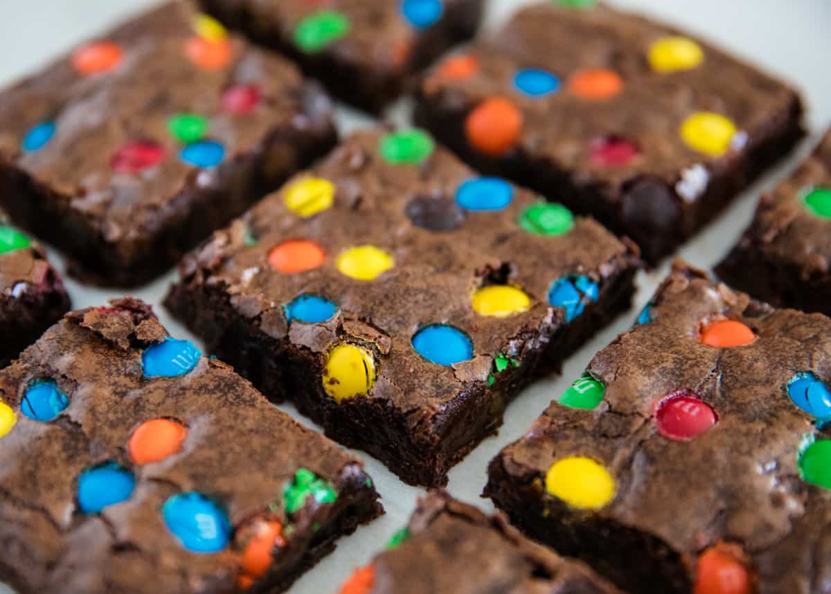 A baking tray with square cut brownies and rainbow colored chocolate candies