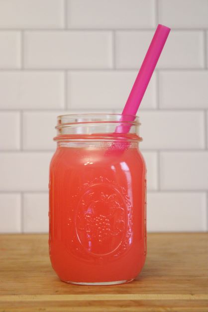 A mason jar with pink lemonade inside along with a pink straw to match