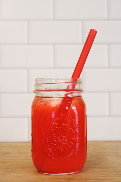 A mason jar with strawberry lemonade along with a matching red straw